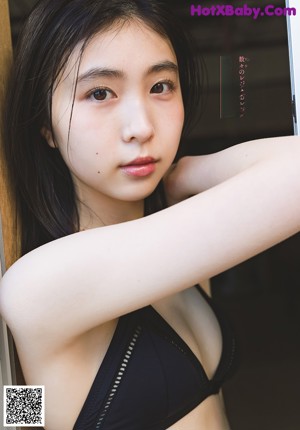 A young woman in a school uniform crouching down on a wall.