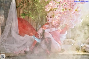 A woman sitting on a rock in front of a flowering tree.