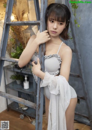 A woman in a gray top and white shorts leaning against a ladder.