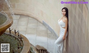 A woman in a green and red dress leaning against a wall.