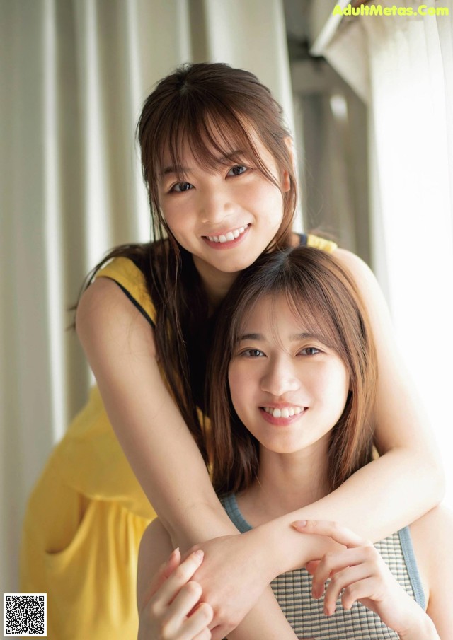 A couple of young women hugging each other in front of a window.