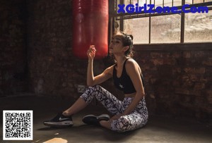 A woman in white leggings and a black tank top holding a yoga mat.