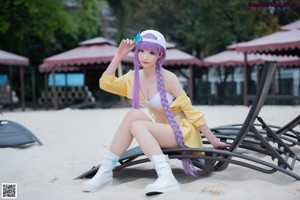 A woman with purple hair sitting on a beach.