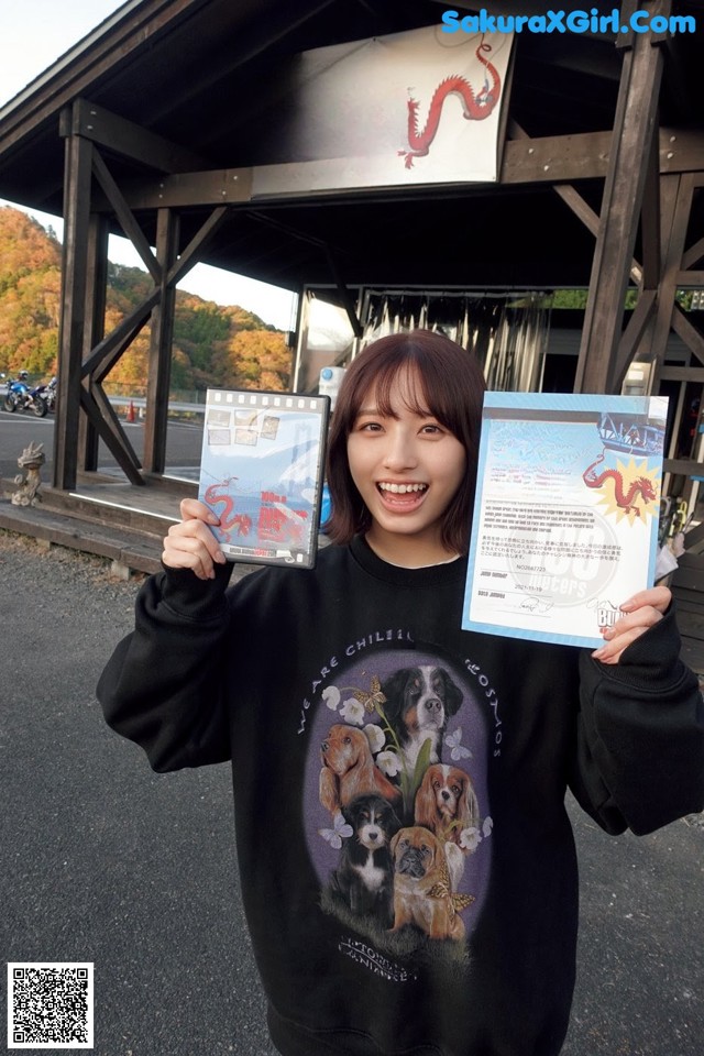A woman holding up two certificates in front of a building.