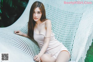 A woman in a white tank top leaning against a wall.