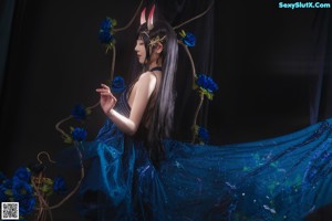 A woman in a blue dress sitting on a bed of blue roses.