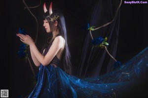 A woman in a blue dress sitting on a chair surrounded by blue roses.