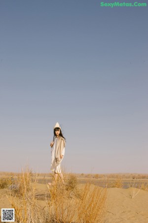 A woman in a white dress and hat sitting in the sand.