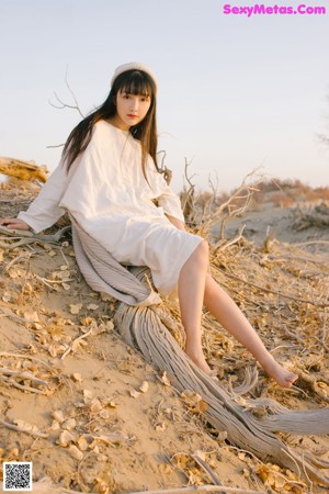 A woman standing in front of a tree wearing a white dress.