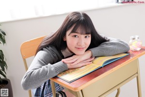 A woman sitting at a desk with a book and a handbag.