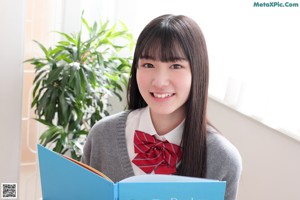 A young woman in a school uniform sitting on a desk.