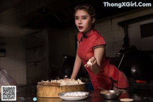 A woman in a red shirt and black skirt preparing food in a kitchen.