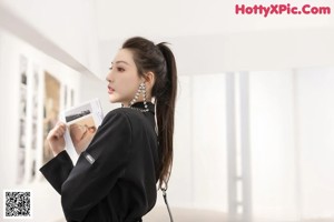 A woman in a black suit standing in a white room.