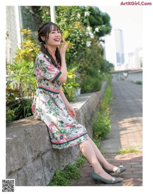 A woman in a floral dress leaning on a railing.