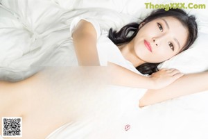 A woman in a white shirt and panties sitting on a bed.