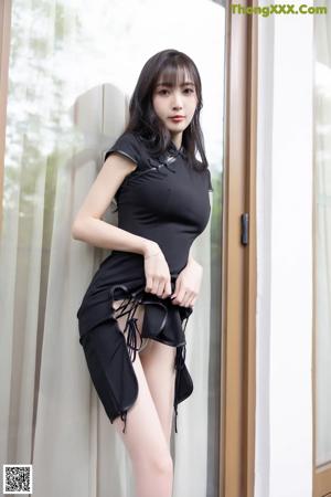 A woman in a black dress sitting on a white couch.
