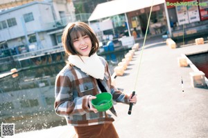 A woman crouching down on the ground wearing a plaid coat.