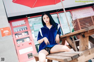 A woman in a blue shirt and black panties crouching down in a store.
