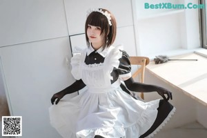 A woman in a maid outfit sitting on a bed holding a broom.