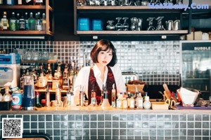 A woman sitting at a bar in a white shirt and black skirt.